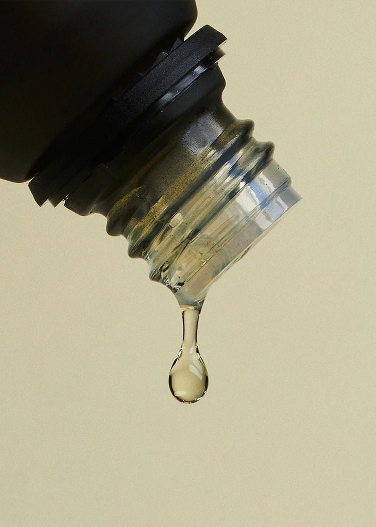 A drop of essential oil falling from the neck of a dark glass bottle